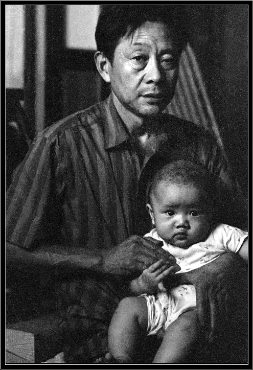 A touching portrait of a grandparent holding a child, both looking solemnly into the camera.